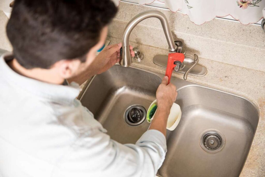 A step-by-step kitchen sink replacement process showing a person removing the old sink and installing a new stainless steel sink with tools and plumbing connections.